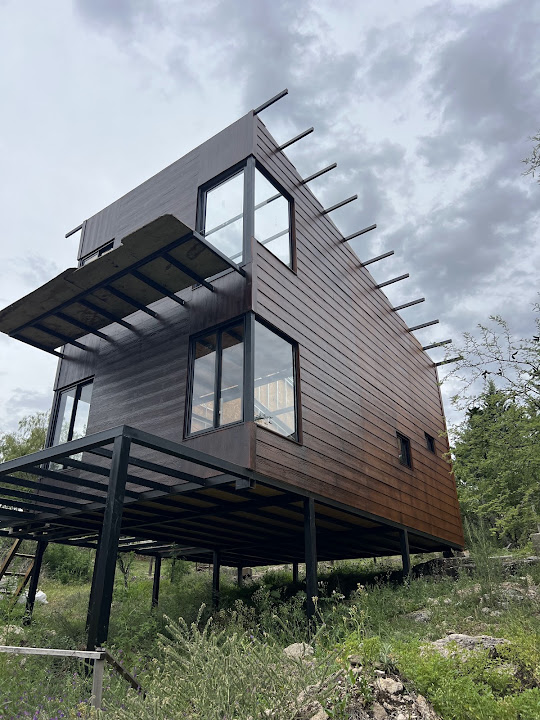 Vivienda elevada con ventanas oscuras y paños vidriados en esquina