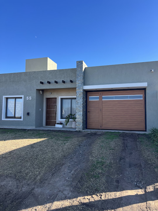 Fachada de vivienda con ventanas bronce colonial, puerta y portón en tonos madera