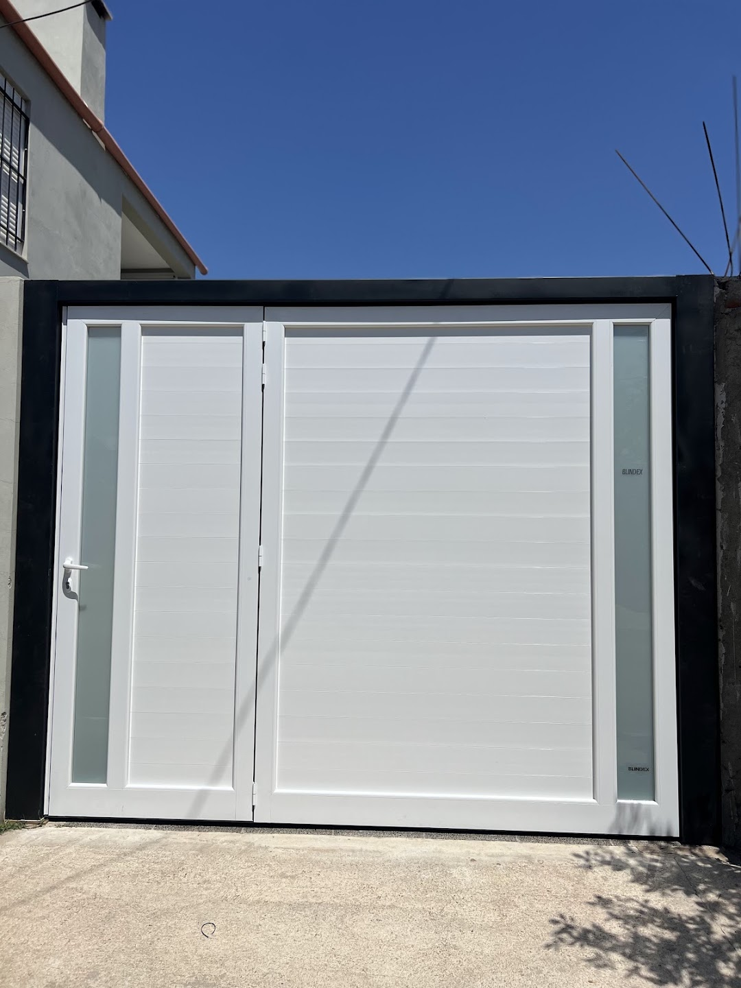 Portón blanco con puerta lateral y dos paños verticales de vidrio opalino blindex