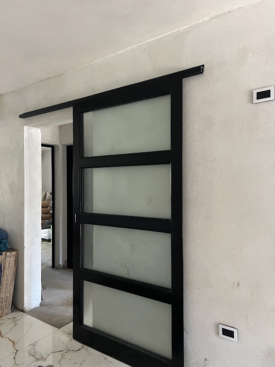 Puerta corrediza negra con tres paños de vidrio translúcido