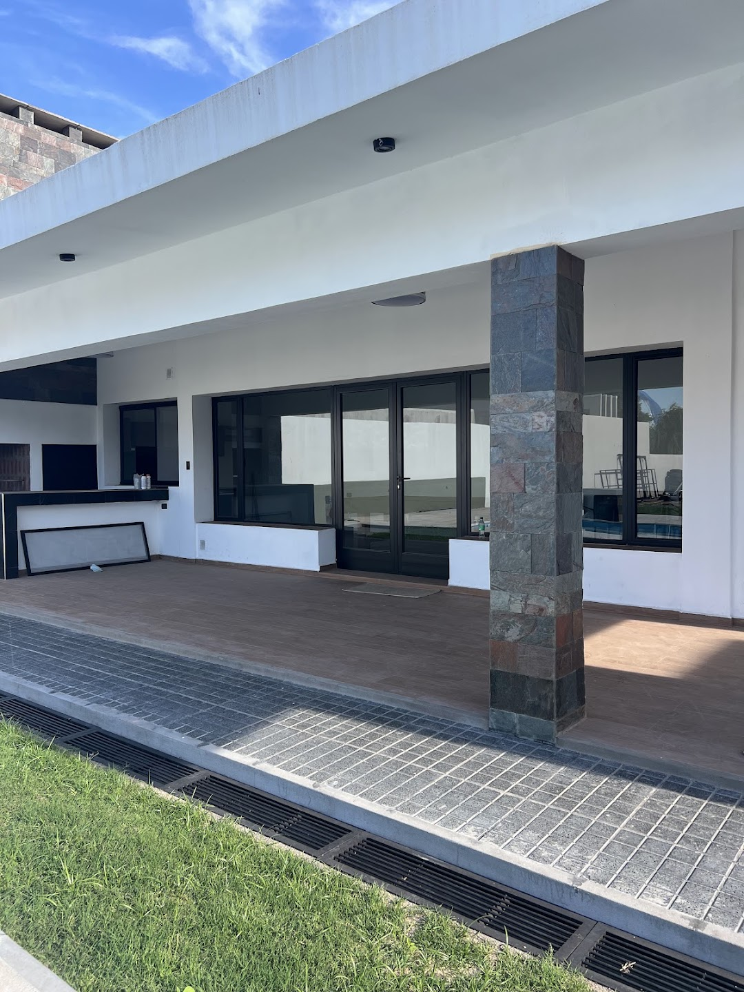 Galería cubierta con puertas y ventanas negras, junto a la pileta