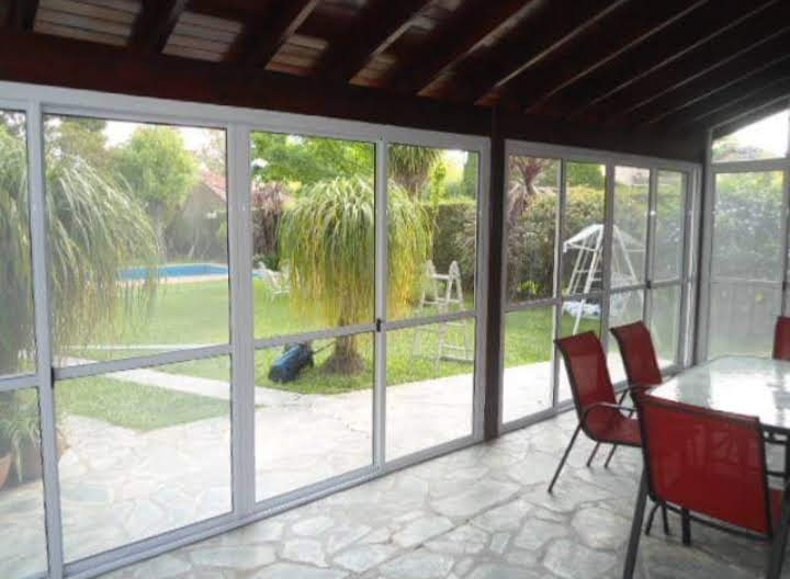 Interior de quincho con cerramiento vidriado blanco y vista al jardín