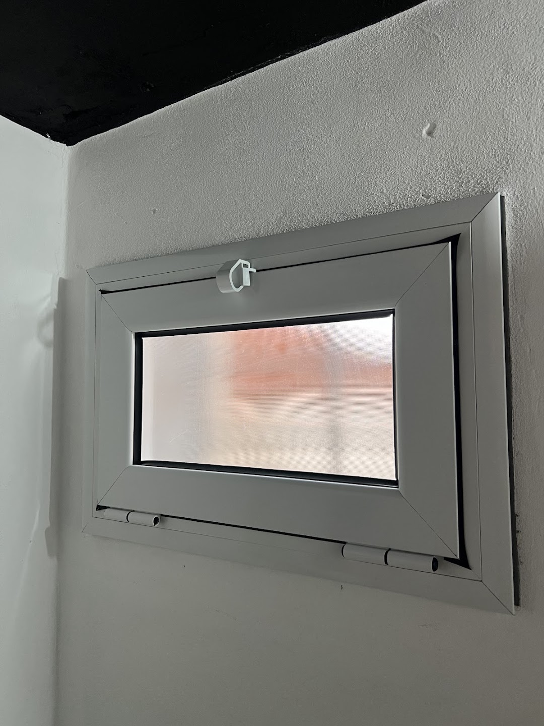 Ventana de formato horizontal con perfiles claros, vidrio translúcido y cierre superior